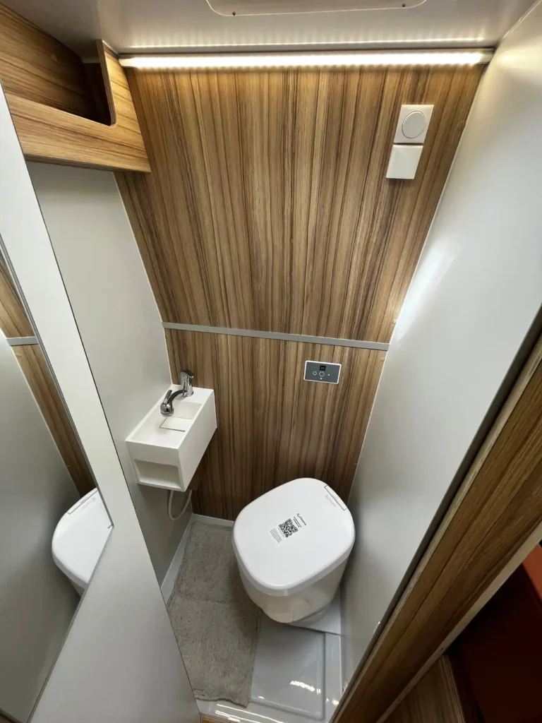 Kompaktowa łazienka w kamperze z toaletą, umywalką i drewnianymi elementami wykończenia