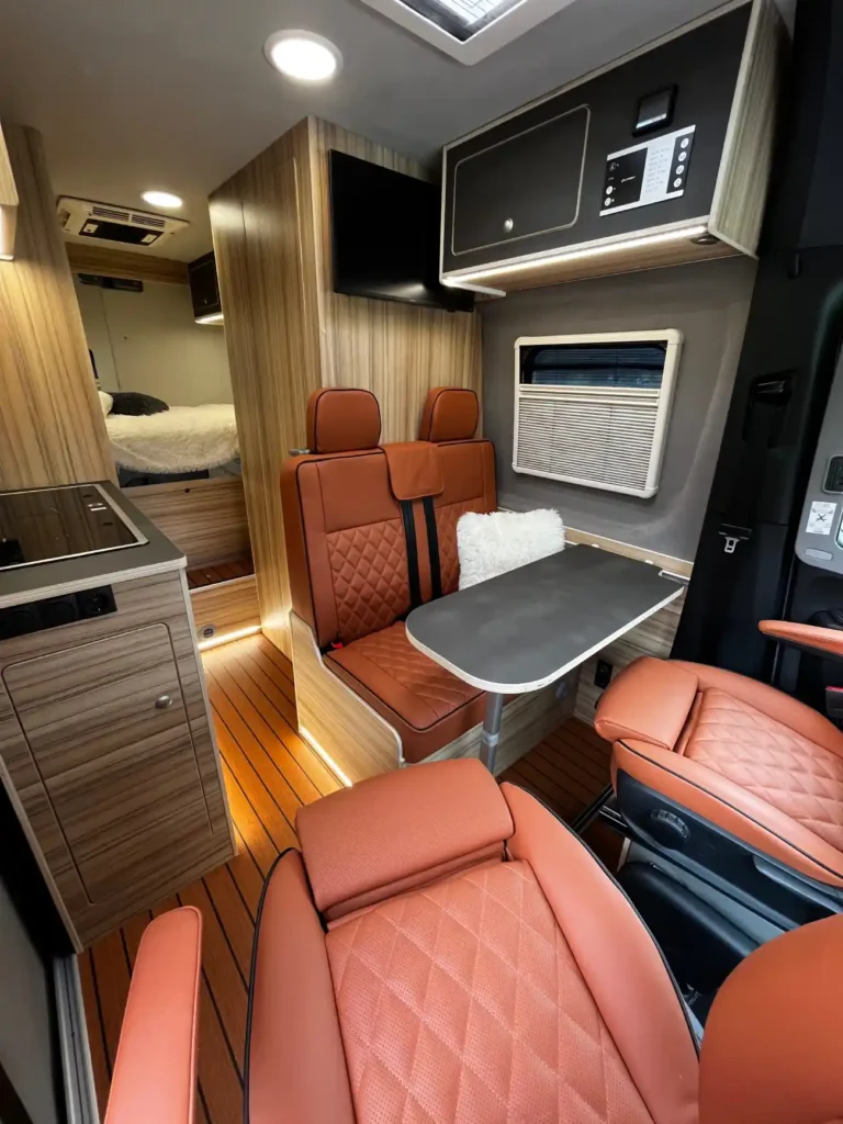 Wnętrze luksusowego kampera z pomarańczowymi skórzanymi siedzeniami, drewnianymi elementami wykończenia i nowoczesnym wyposażeniem